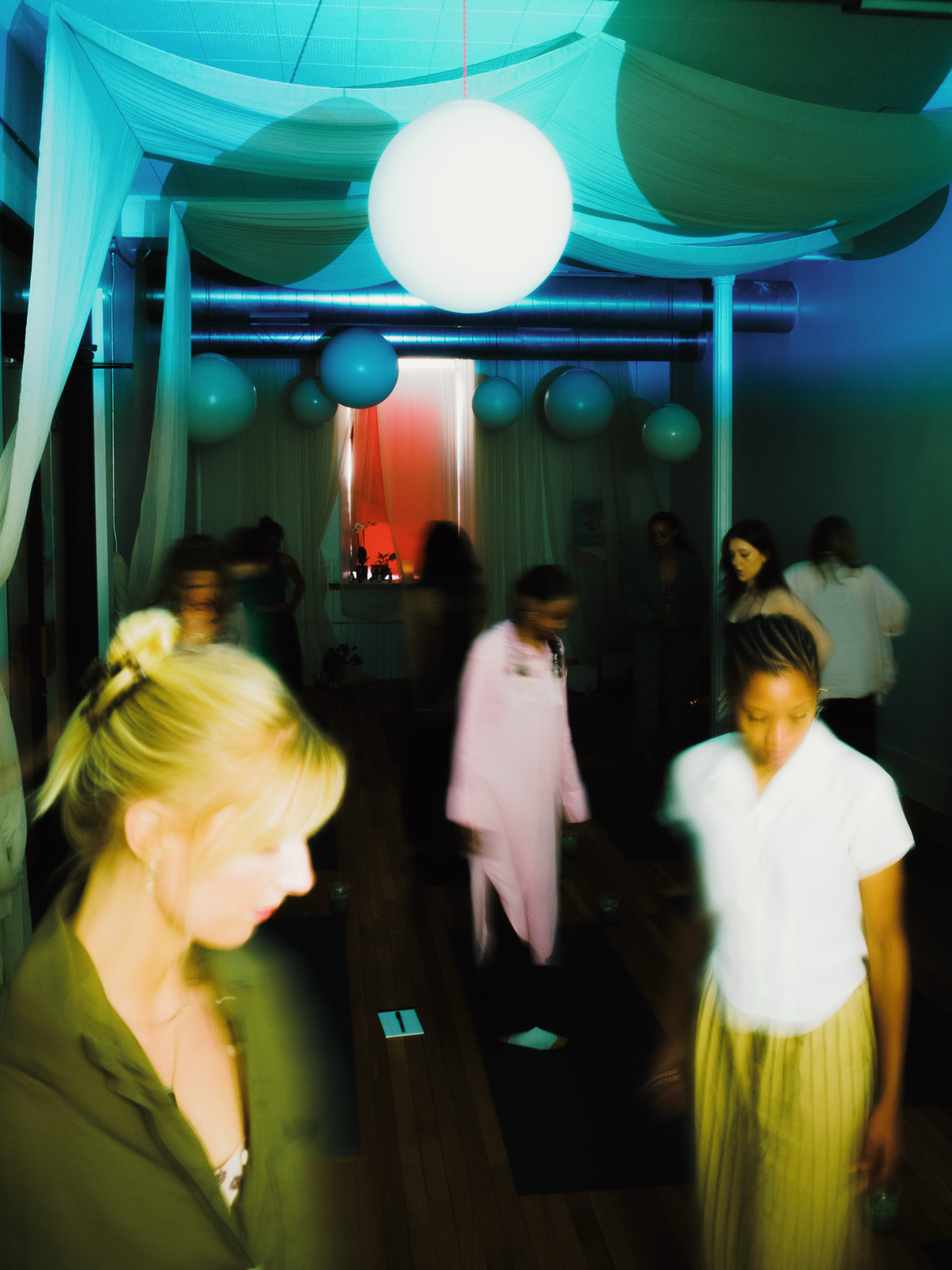 A class moving through the yoga room in teal and pink light under paper lanterns