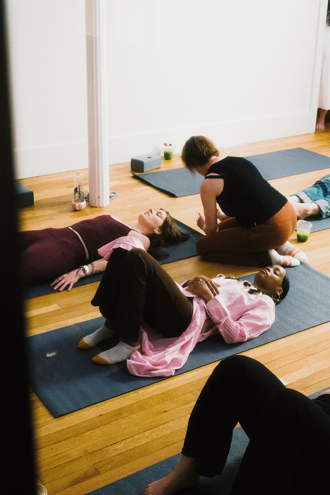 People resting on mats in the yoga room while a practitioner kneels beside them